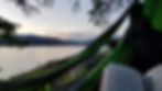 A book is open on the lap of a person in a hammock. In the background is a peaceful lake and Sugarloaf Mountain.